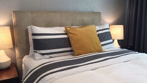 Una cama bien hecha con ropa de cama a rayas y una almohada de color mostaza.