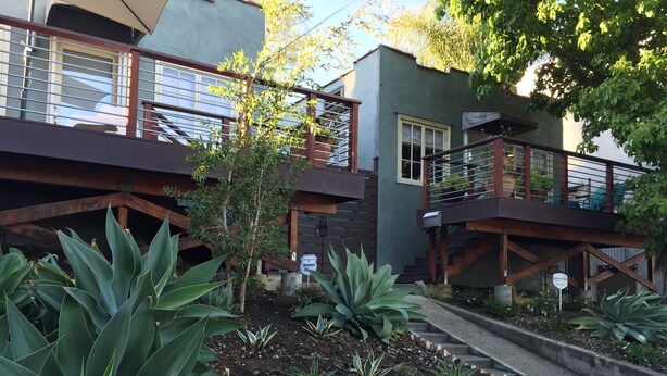 Un edificio residencial con balcón, escaleras y un jardín con diversas plantas.