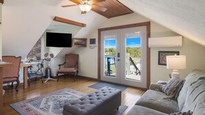 A cozy attic bedroom with a ceiling fan, a large window with a view, a bed, and a desk with a chair. - The Narrow’s Yacht Club Emilia’s Loft (Lake Leelanau)