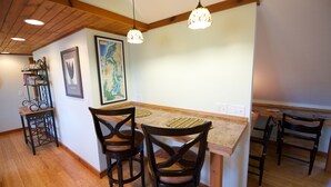 A kitchen with wooden flooring, a bar area with two chairs, pendant lights, and a map on the wall. - The Narrow’s Yacht Club Emilia’s Loft (Lake Leelanau)