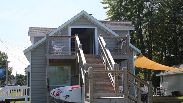 A two-story house with a wooden deck and a small staircase leading to a balcony. - The Narrow’s Yacht Club Emilia’s Loft (Lake Leelanau)