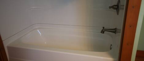 Una bañera blanca con grifo y ducha, frente a una pared de azulejos.