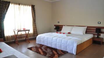 Una habitación de hotel con una cama grande, una mesita de noche, una pequeña mesa y un ventanal con cortinas.