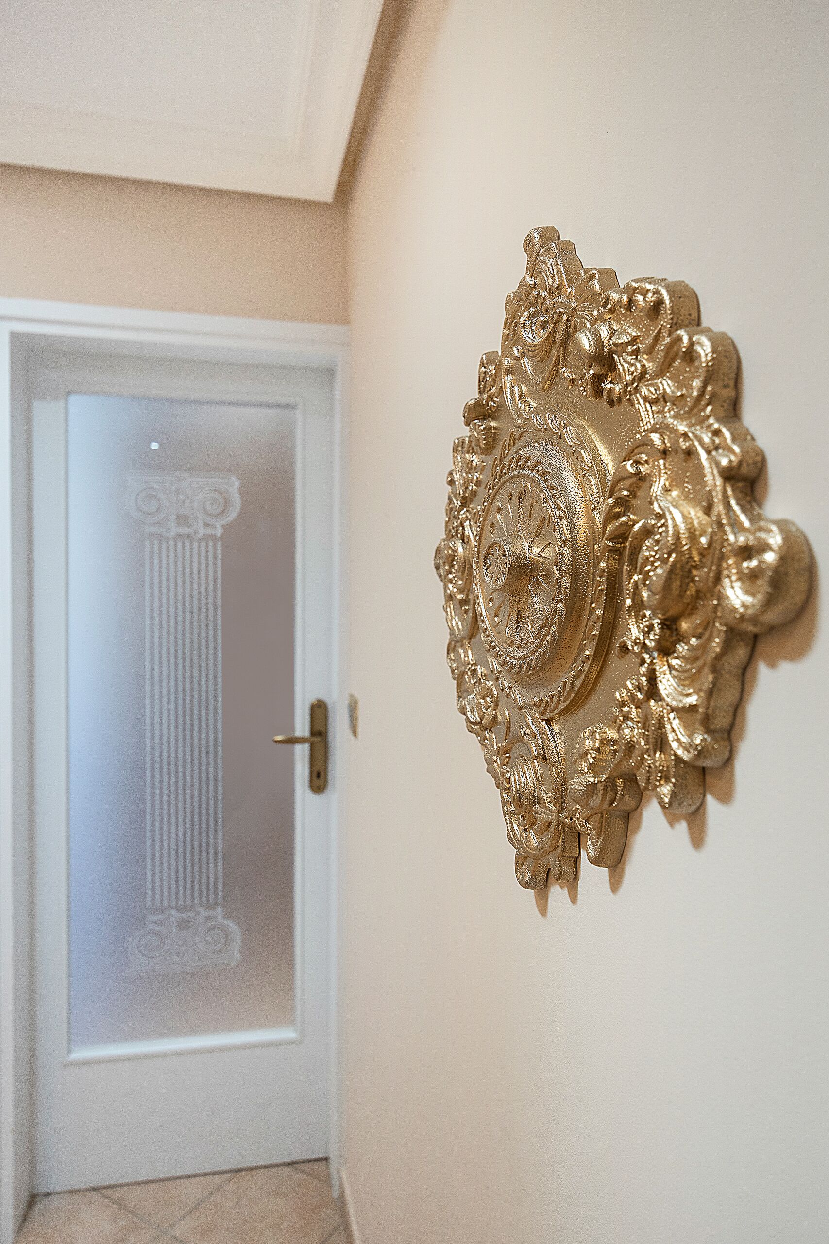 A room with a white door featuring a glass panel and a decorative gold mirror on the wall.