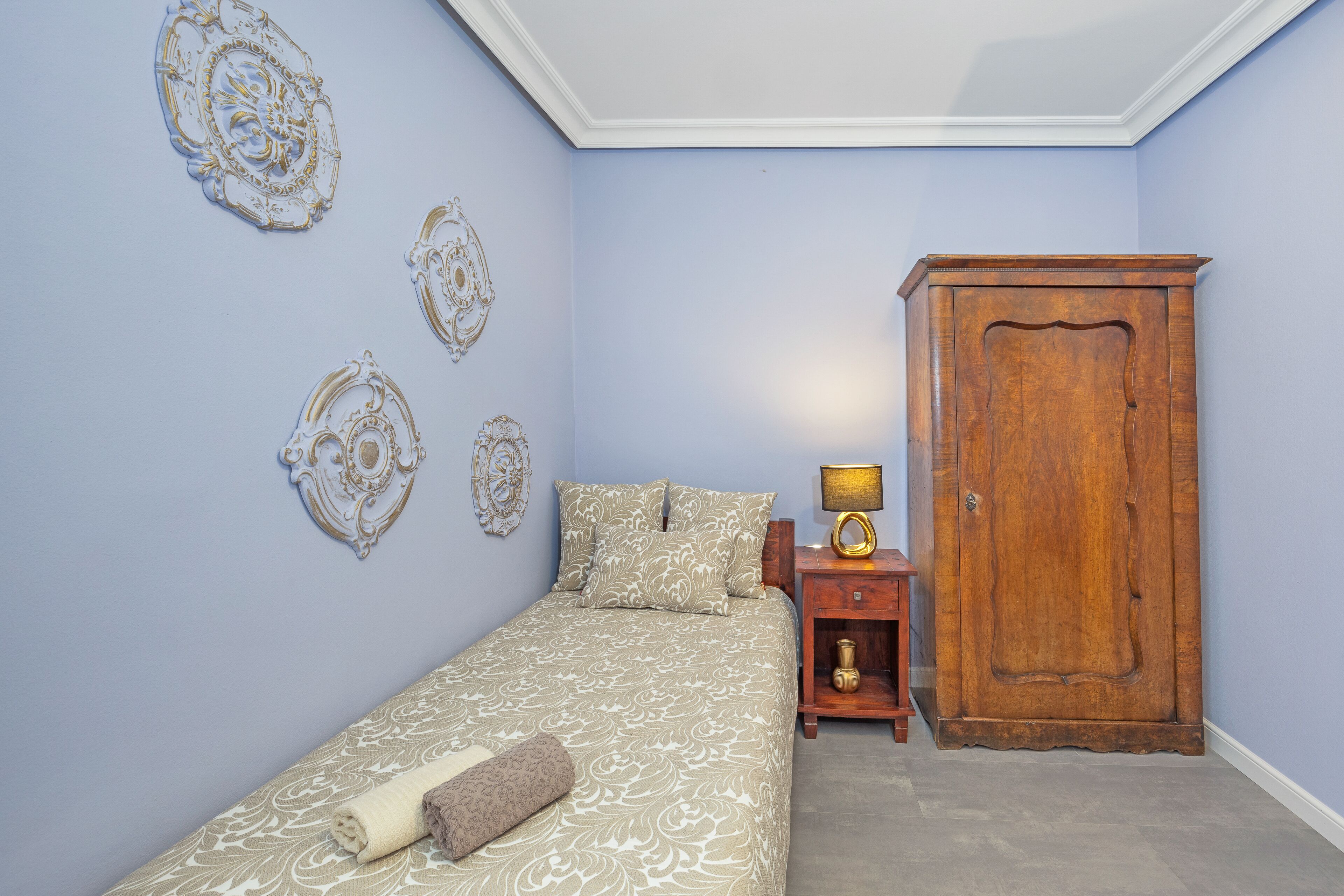 A bedroom with a bed, a wooden wardrobe, a nightstand with a lamp, and decorative wall art.