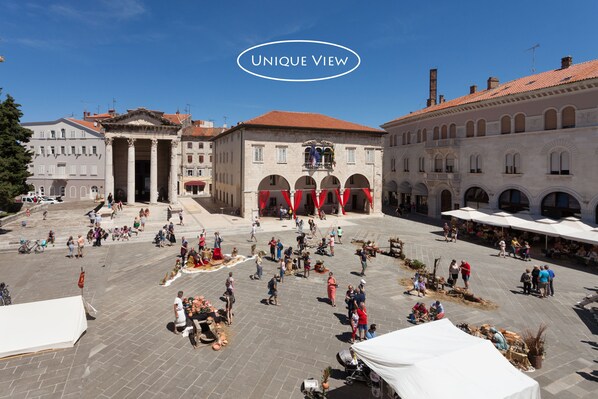 A spacious public square with historical buildings, open-air market stalls, and a clear blue sky.