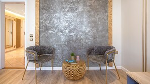 A room with two grey upholstered chairs, a round woven coffee table, and a textured grey wall. - Augustus Forum View (Pula)
