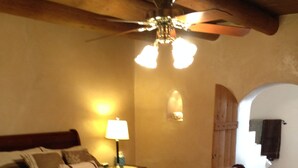 A bedroom with a wooden bed, a nightstand with a lamp, a ceiling fan, and a tiled floor.