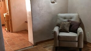 A living room with a wooden table, a beige armchair with a pillow, and a small alcove with a window.