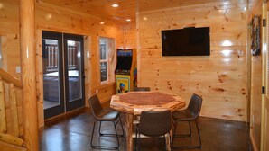 A wooden interior with a round table and four chairs, a television mounted on the wall, and a game machine. - Luxury 5 King Suites, 5 Bath Log Cabin Close to Town & Trolley (Gatlinburg)