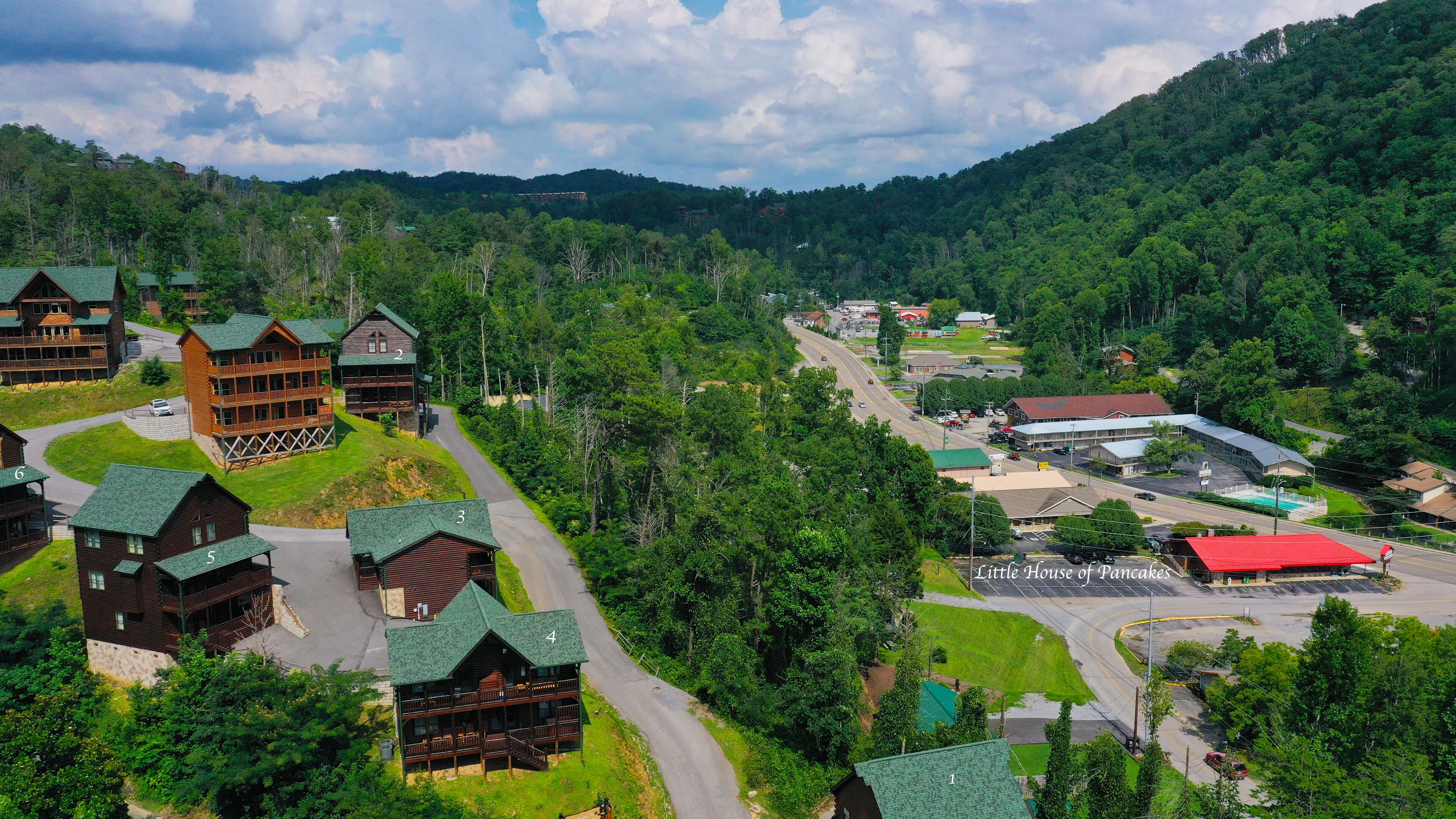 A lodge with multiple wooden cabins, a main building with a red roof, and a road leading through a forested area.