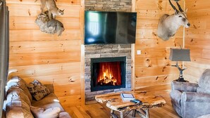 A cozy cabin interior with a stone fireplace, wooden walls, and two leather sofas. - Luxury 5 King Suites, 5 Bath Log Cabin Close to Town & Trolley (Gatlinburg)