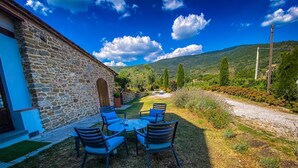 Un bâtiment en pierre doté d’une table et de chaises sur une terrasse, entouré d’un jardin et offrant une vue sur la campagne.