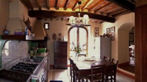 Une cuisine équipée d’une cuisinière à gaz, d’un évier et de meubles de rangement en bois. On y trouve une table à manger avec des chaises et un lustre au-dessus.