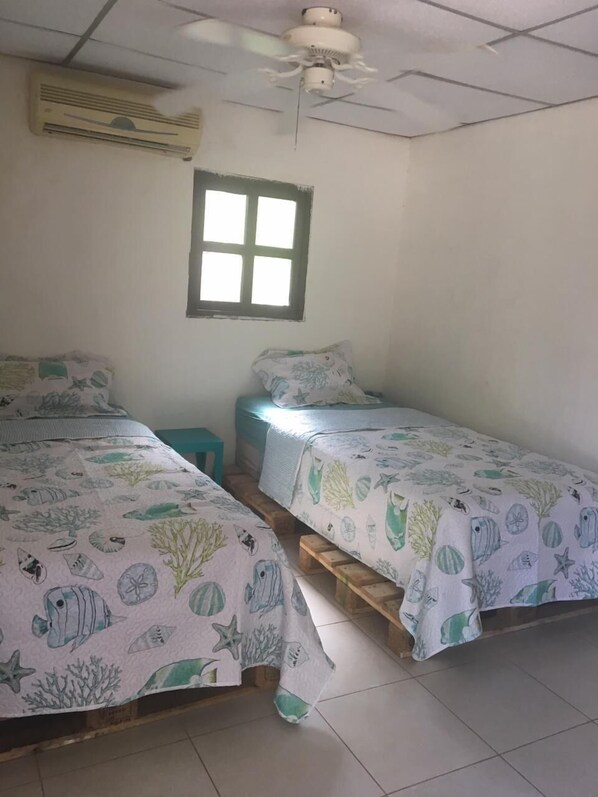 A room with two beds, each with a sea-themed bedspread, a window, and a ceiling fan.