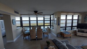 Un salón espacioso con un ventanal grande que da a un lago, muebles de mimbre, un ventilador de techo y un televisor.