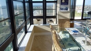 Un balcón amplio con vistas a la ciudad, mobiliario de mimbre y una mesa de vidrio.