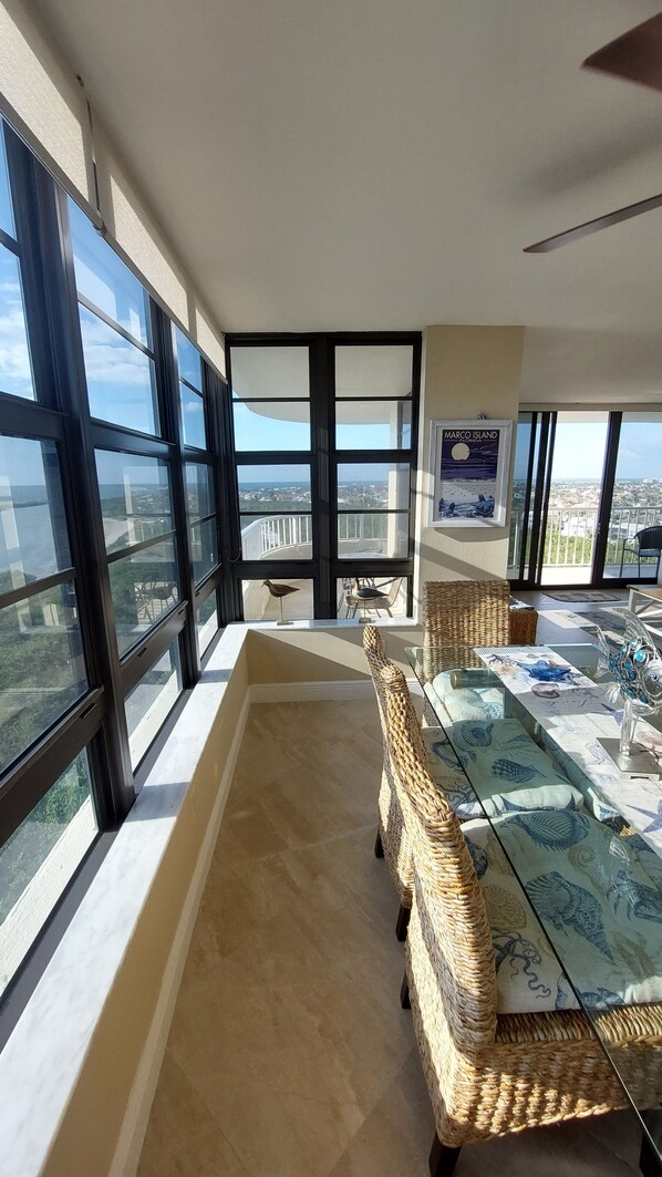 A spacious balcony with a view of the city, wicker furniture, and a table with a glass top. - Beautiful, Oceanfront South Seas NW Condo with Stunning Views (Marco Island)