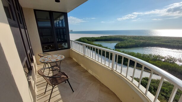 Un balcón con vistas a un río y a la costa distante, una mesita y una silla.
