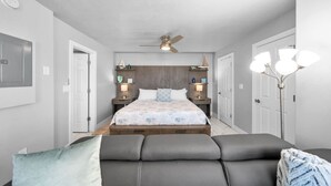 Une chambre à coucher comprenant un lit, des tables de chevet, un ventilateur de plafond et une lampe sur pied.