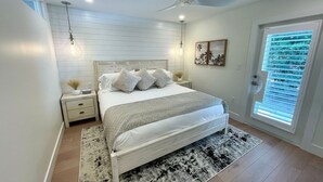 Une chambre à coucher comprenant un lit, des tables de chevet, un ventilateur de plafond, une fenêtre avec des stores et un luminaire fixé au mur.