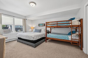 Une chambre avec un lit superposé, un lit simple, une fenêtre avec des rideaux, une lampe et un élément de décoration murale.