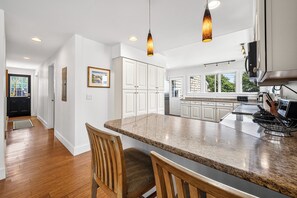 Cozinha moderna com armários brancos, bancada de granito e iluminação pendente.