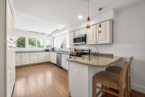 A modern kitchen with white cabinetry, a central island, and pendant lighting. - Private, 1st Floor Cottage, 5 Minute Walk to Beach- Perfect for Families! (Old Orchard Beach)