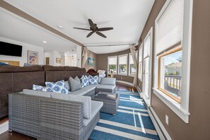 Uma sala de estar espaçosa com sofá modular, ventilador de teto e janelas amplas.