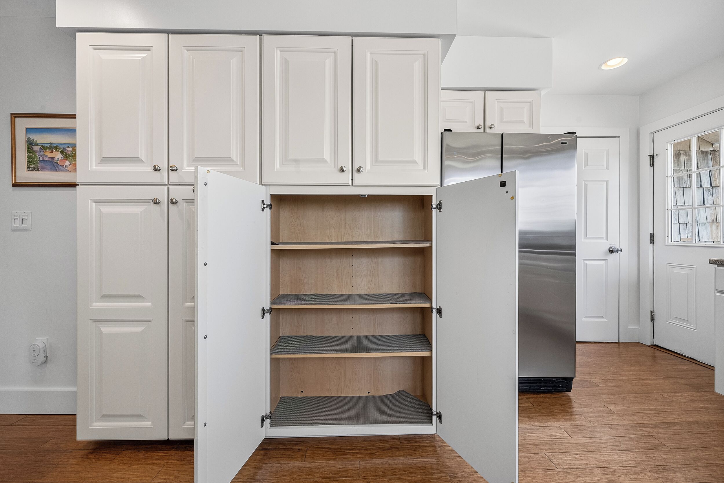 A kitchen with white cabinets, a stainless steel refrigerator, and a wooden floor.