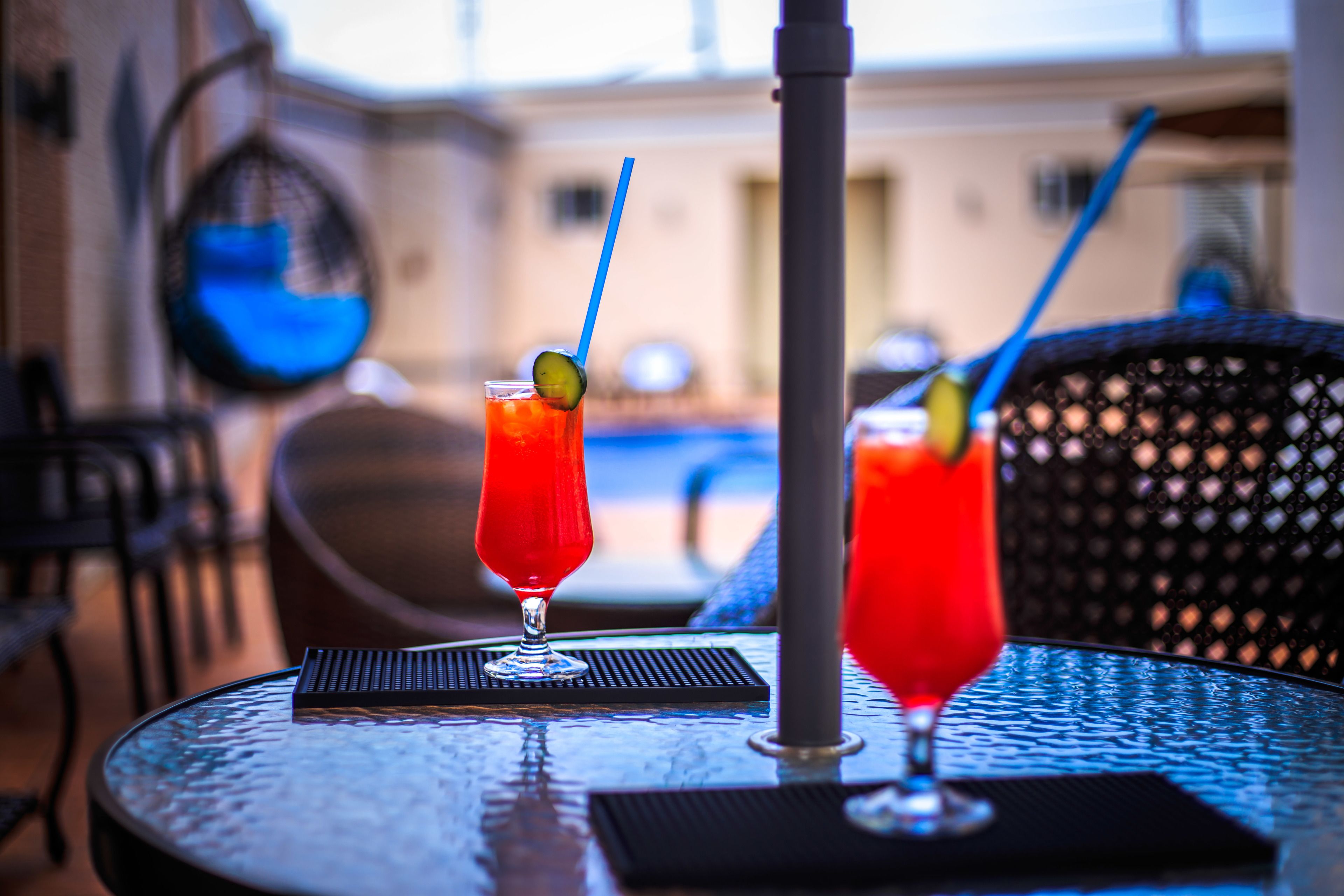 Two drinks on a table with a pool in the background.