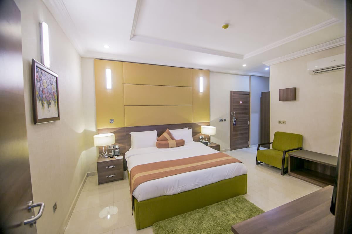 A hotel room with a large bed, bedside tables, a green chair, and a desk.