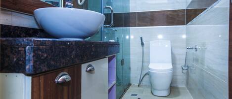 A modern bathroom with a glass shower enclosure, a white toilet, and a marble countertop with a bowl sink.