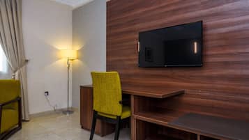 A modern room with a wooden wall, a flat-screen TV, a yellow chair, a desk, and a floor lamp.