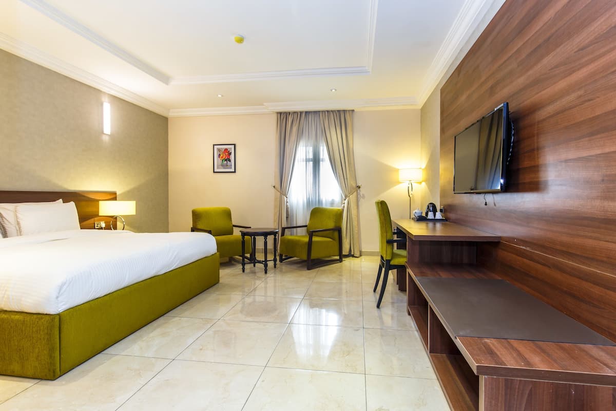 A hotel room with a bed, a desk, a chair, a TV mounted on the wall, and a window with curtains.