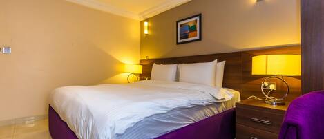 A hotel room with a large bed, two bedside tables with lamps, a small desk, and a chair.