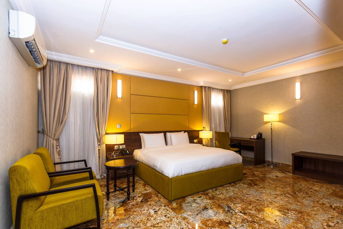 A hotel room with a bed, a desk, a chair, and a lamp.