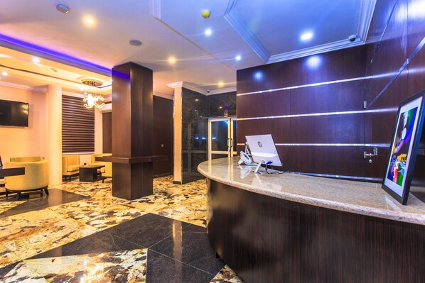 A reception area with a marble floor, wooden reception desk, and a mounted laptop.