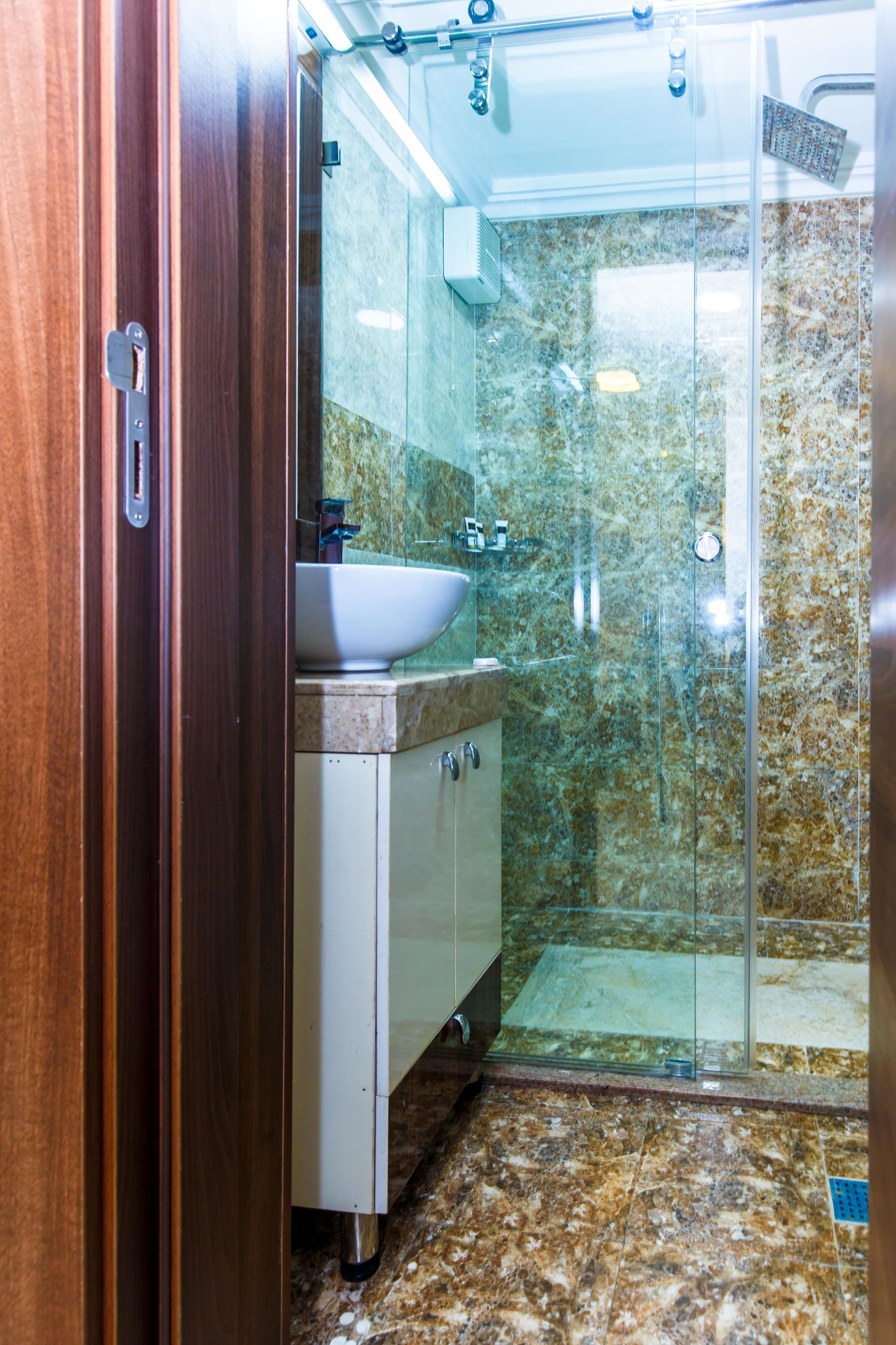 A bathroom with a glass shower enclosure, a sink, and a marble-tiled wall.