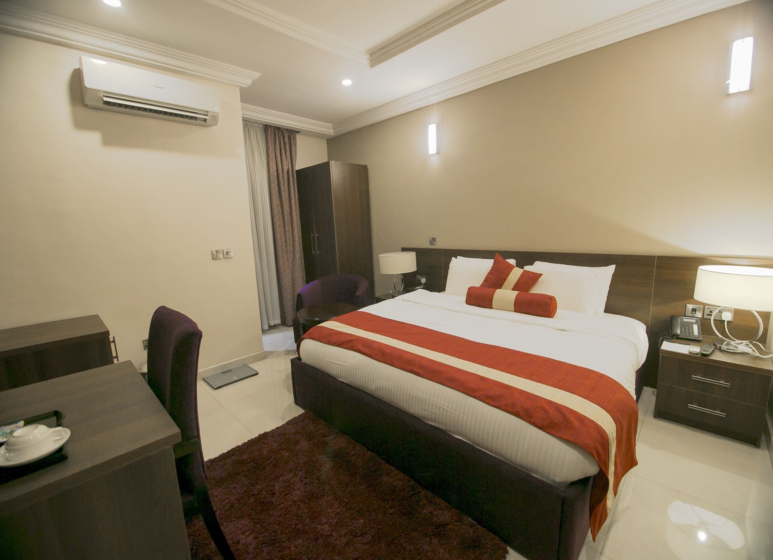 Una habitación de hotel con cama, mesita de noche, lámpara y escritorio con silla.