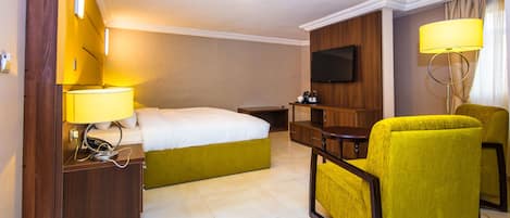 A hotel room with a bed, bedside table, lamp, chair, TV, and a small table.