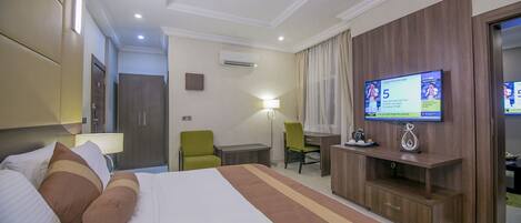Habitación de hotel con una cama grande, un escritorio, una silla, un televisor y un armario.