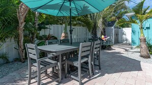 A patio with a table and chairs, surrounded by a white fence and palm trees. - Steps To The Beach, Private & Heated Pool, Renovated - Now Booking Summer/Fall! (Holmes Beach)