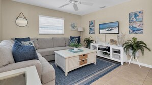 A living room with a beige sofa, a white coffee table, a ceiling fan, and artwork on the walls. - Steps To The Beach, Private & Heated Pool, Renovated - Now Booking Summer/Fall! (Holmes Beach)