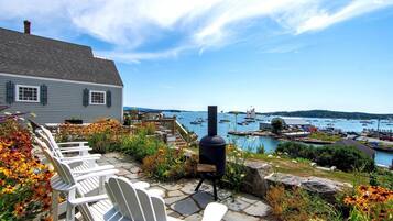 A patio with Adirondack chairs, a wood stove, and a view of a harbor with boats.