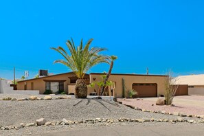 A modern two-story house with a flat roof, a garage, and a landscaped front yard with rocks and palm trees. - Tropical Paradise! Walking distance to Bridge/Channel! Huge Yard & Heated Pool (Lake Havasu City)
