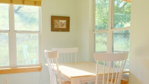 A dining area with a table and four chairs, large windows with a view of greenery, and a framed picture on the wall. - Papa's Palace at Stacy Ranch, cabin on 120 acres between Ingram & Hunt, TX (Ingram)