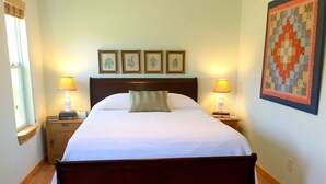 A neatly made bed with a wooden headboard, two bedside lamps, and framed botanical prints on the wall. - Papa's Palace at Stacy Ranch, cabin on 120 acres between Ingram & Hunt, TX (Ingram)