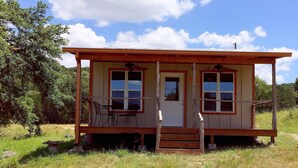 A small, single-story house with a porch, two windows, and a door. - Papa's Palace at Stacy Ranch, cabin on 120 acres between Ingram & Hunt, TX (Ingram)