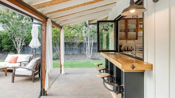 Ein überdachter Außenbereich mit Bar, Sitzgelegenheiten und Blick auf den Garten.